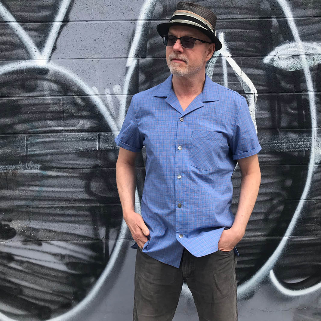 Men's Tropical Shirt,Papierschnitt,Wardrobe by me,Mann mit Sonnenbrille und Hut in blauem Hemd vor Mauer